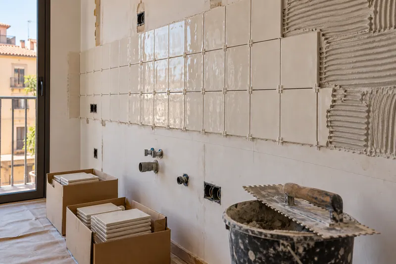 Visualización conceptual IA: Colocación de azulejos con separadores y adhesivo sobre una pared de cocina.